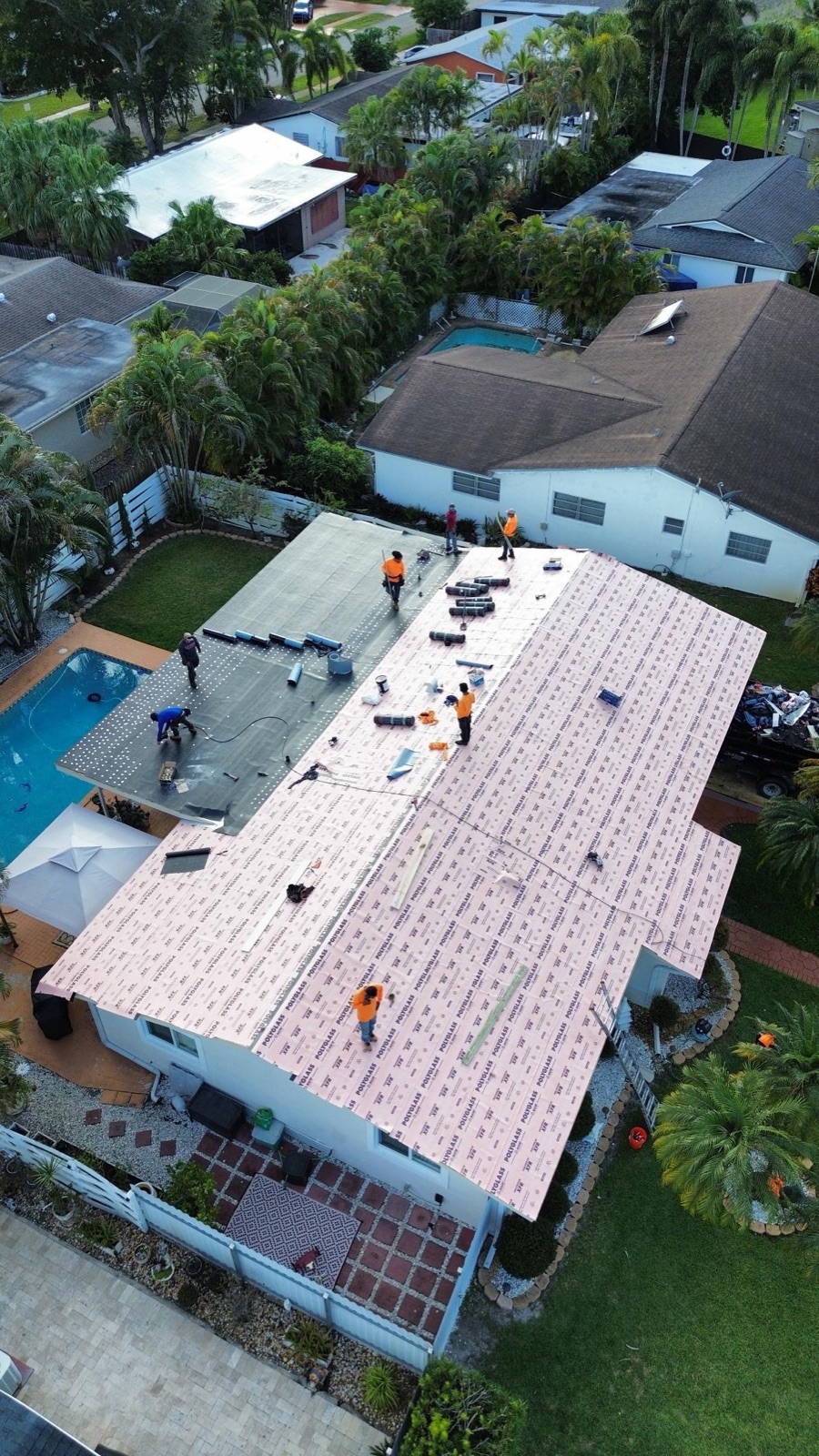 Aerial of roofing crew installing residential roof near pool
