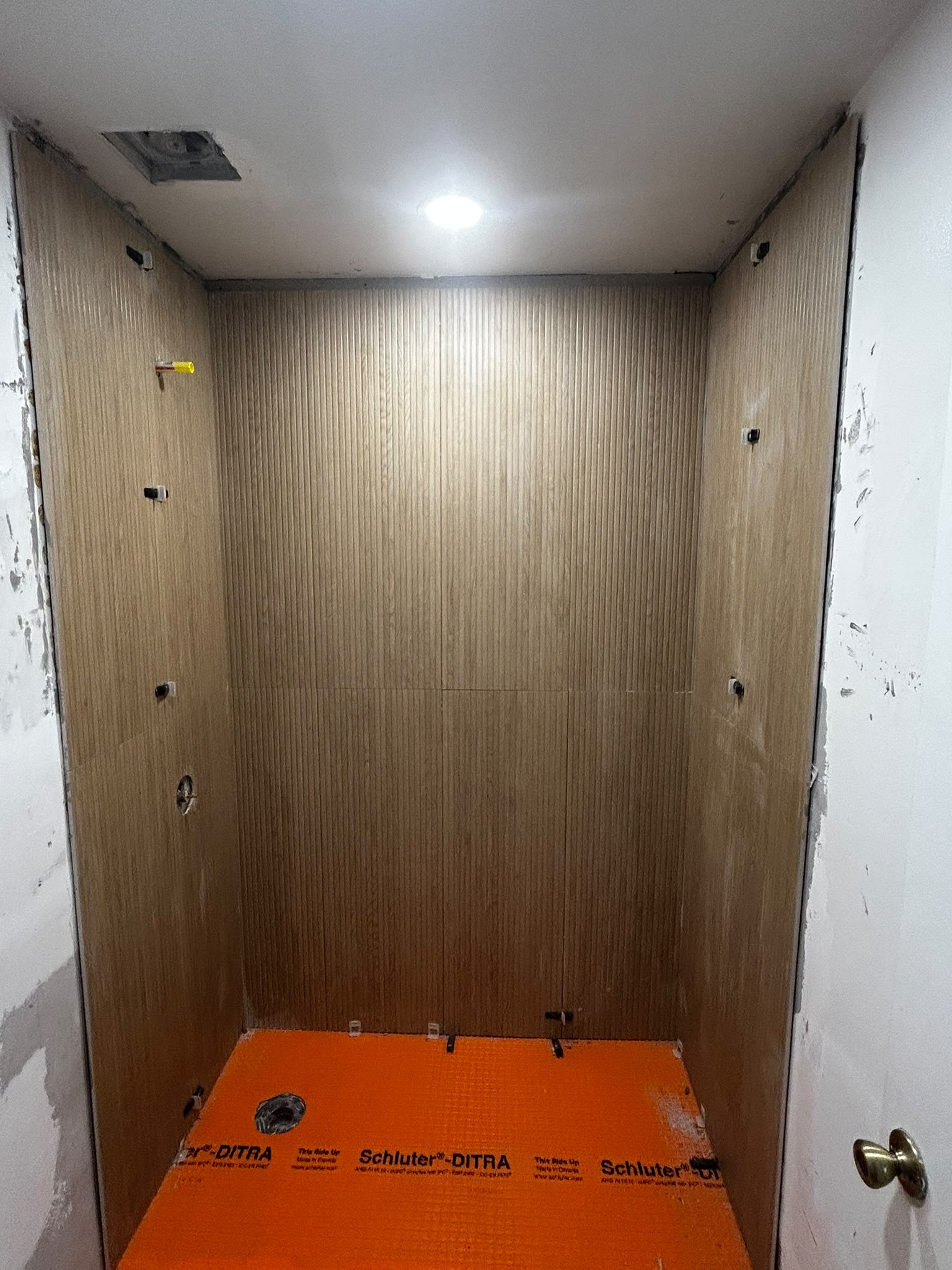Shower with wall tile installed and orange uncoupling membrane on floor